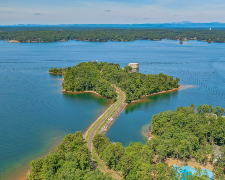 Narrow road links forested shore to island with one building.