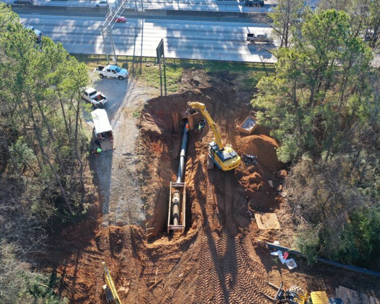 Vista aérea de trabajadores y maquinaria instalando tuberías cerca de la carretera.