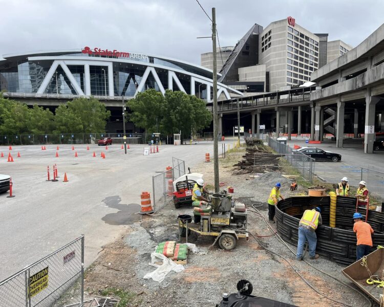 Unos trabajadores instalan la infraestructura en el aparcamiento; al fondo se ve el State Farm Arena.