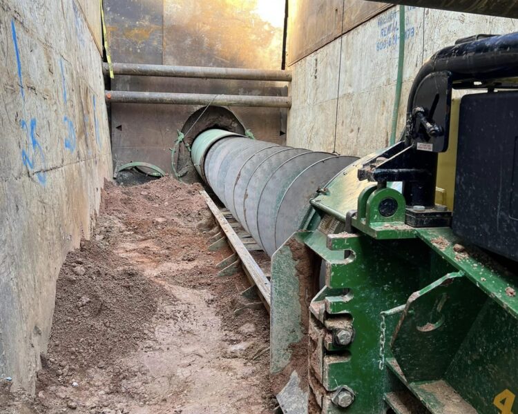 Una gran perforadora de tornillo sinfín excava una zanja en tierra compactada entre la maquinaria.