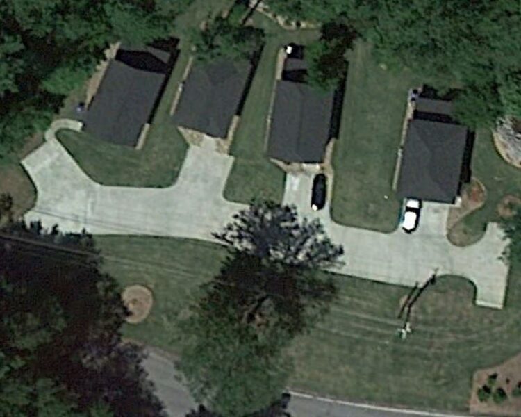 Three houses with driveways and cars, surrounded by trees.