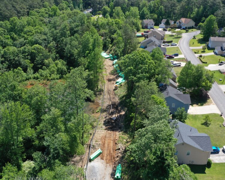 Aerial view: cleared utility path and materials between neighborhood homes.