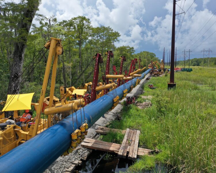 Unos trabajadores instalan una tubería azul con maquinaria junto a las líneas eléctricas.