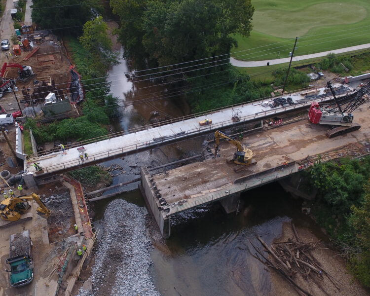 Puente en construcción sobre el río, con vehículos y trabajadores.