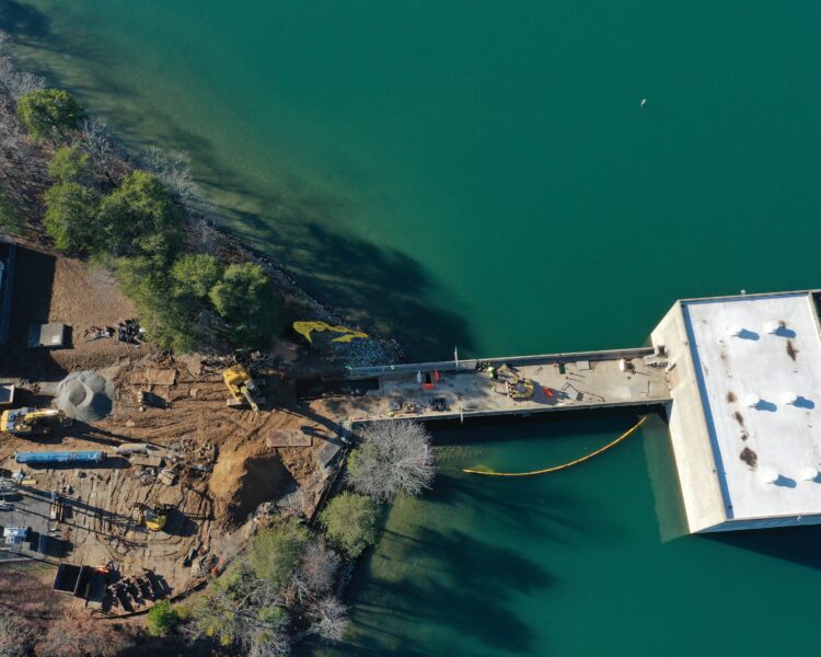 Shoreline construction site with workers, equipment, and blue-green water.