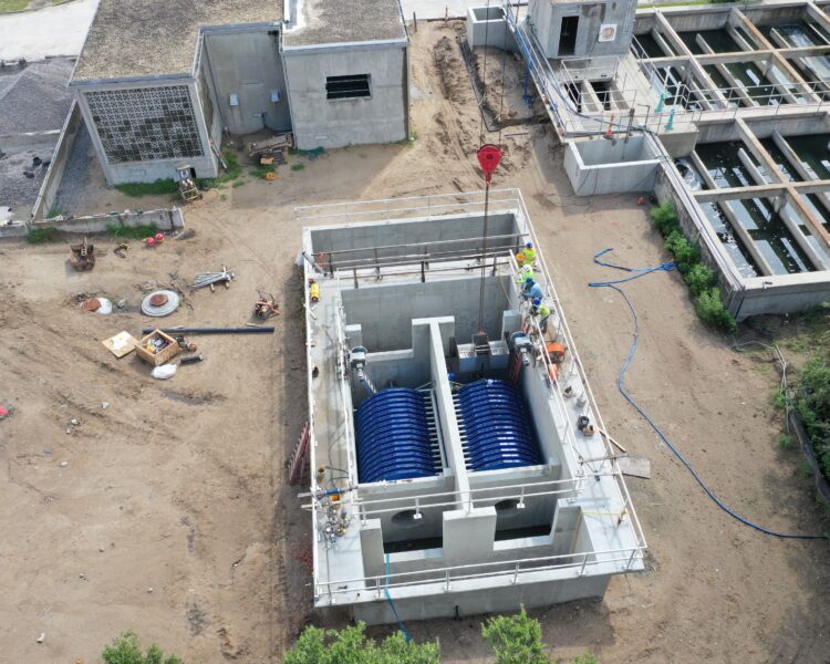 Vista aérea de unos trabajadores instalando equipos azules en una planta de tratamiento de aguas.