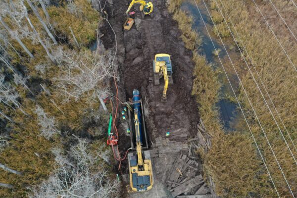 Las excavadoras y los trabajadores excavan en un terreno embarrado cerca de humedales y líneas eléctricas.