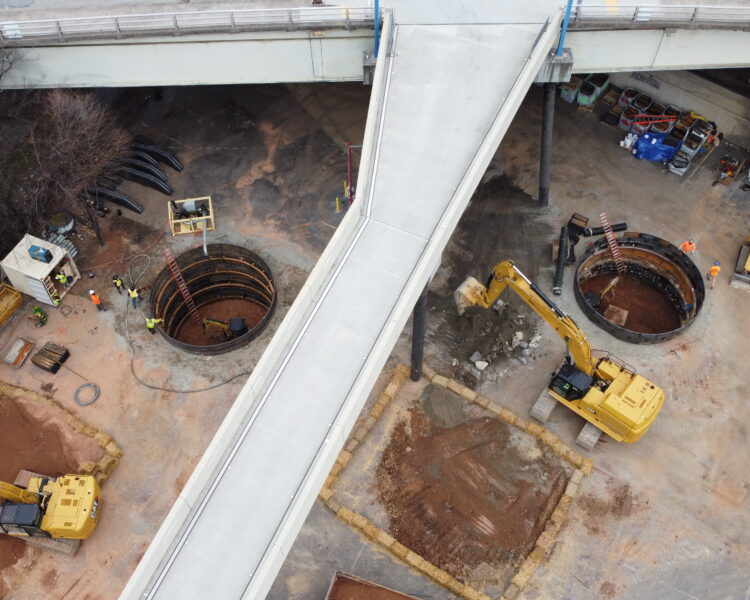 Vista aérea: dos excavaciones circulares, maquinaria, trabajadores, pasarela de hormigón.