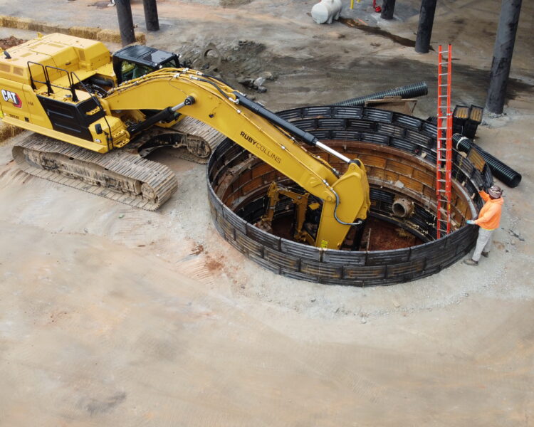 Un obrero de la construcción junto a una gran excavadora en un foso circular con una escalera roja.
