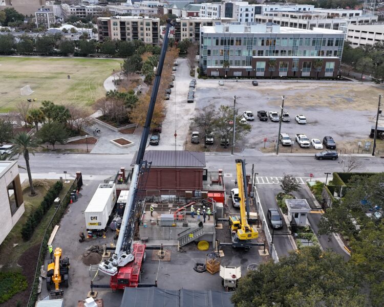 Aerial view: construction site, cranes, sports field, parking lot.