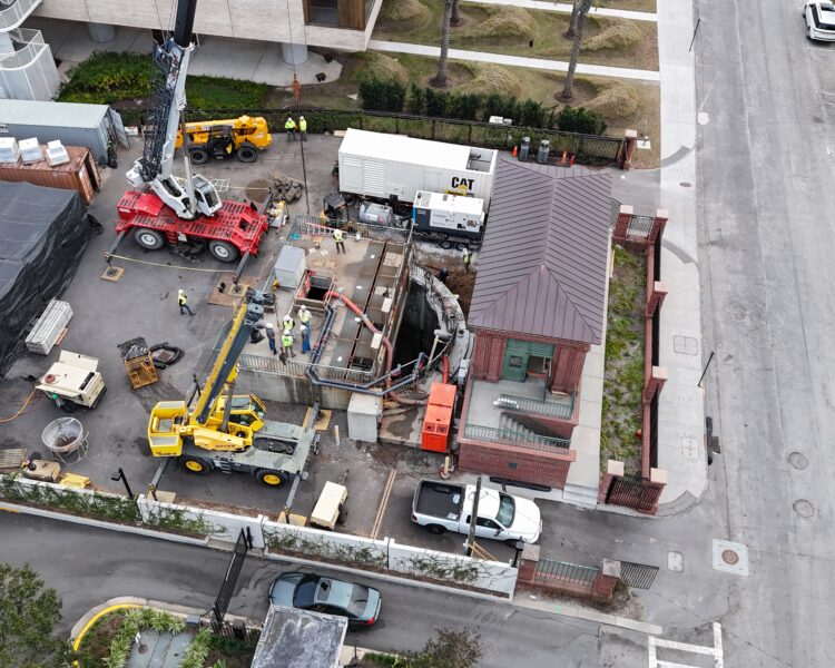 Construction site aerial with workers, cranes, vehicles, and brick building.