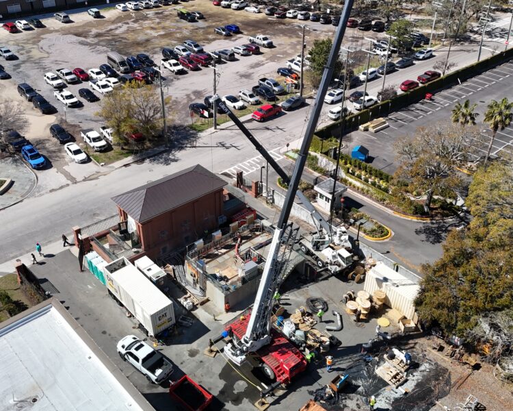 Aerial view: construction site, cranes, vehicles, parking lot, trees.