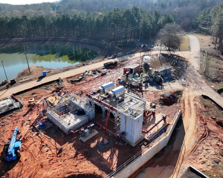 Aerial view of construction site with pond, trees, and machinery.