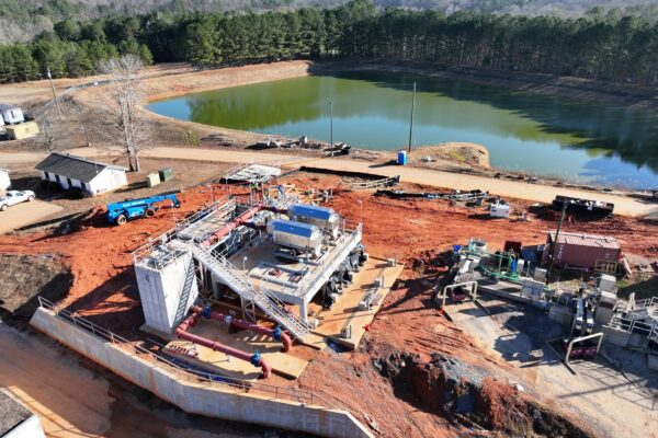 Obra en construcción, maquinaria junto a un estanque, árboles y caminos de tierra en las inmediaciones.