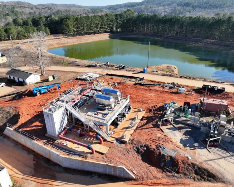 Construction site, machinery by pond, trees and dirt roads nearby.