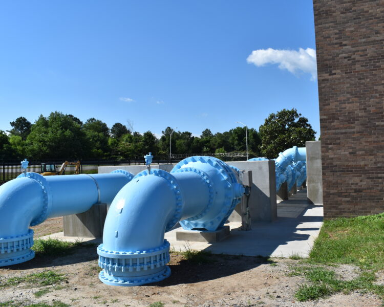 Tuberías de agua azules junto a un edificio de ladrillo, con hormigón y vegetación.