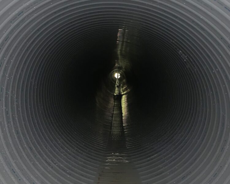 Túnel de chapa ondulada con escalera, iluminado en el extremo más alejado.