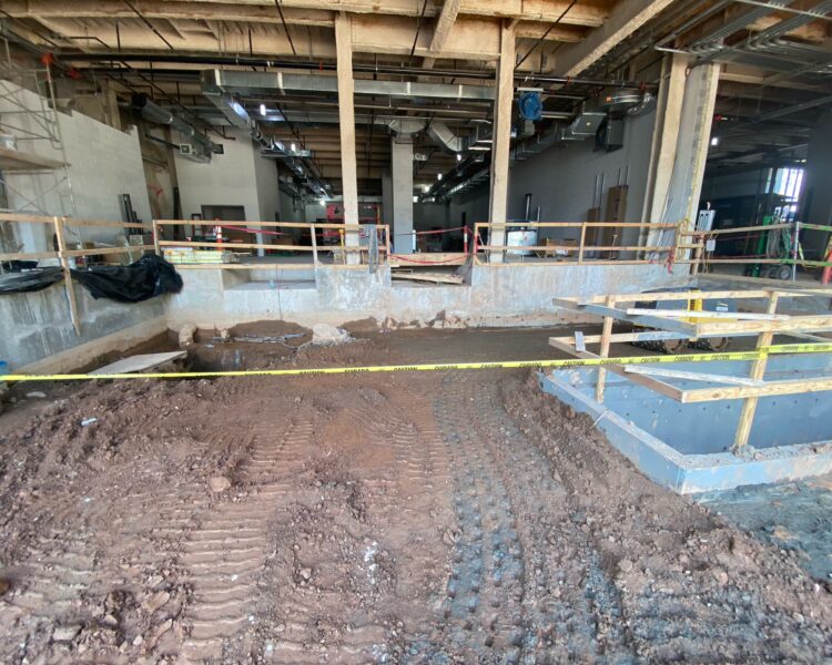 Exposed beams, dirt floor, caution tape in unfinished construction site.