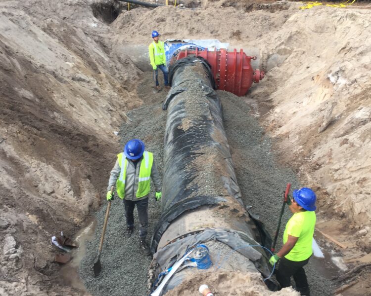 Construction workers install a large pipe in a dirt trench.
