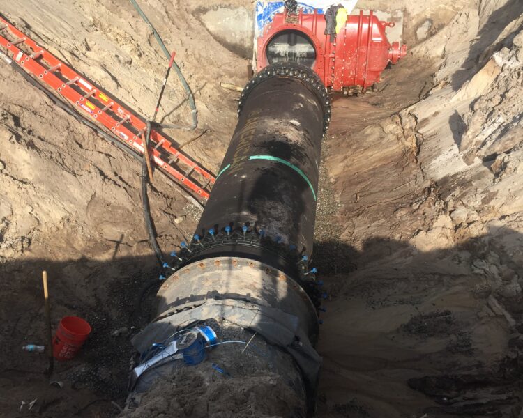 Underground pipe and red valve exposed amid dirt and equipment.