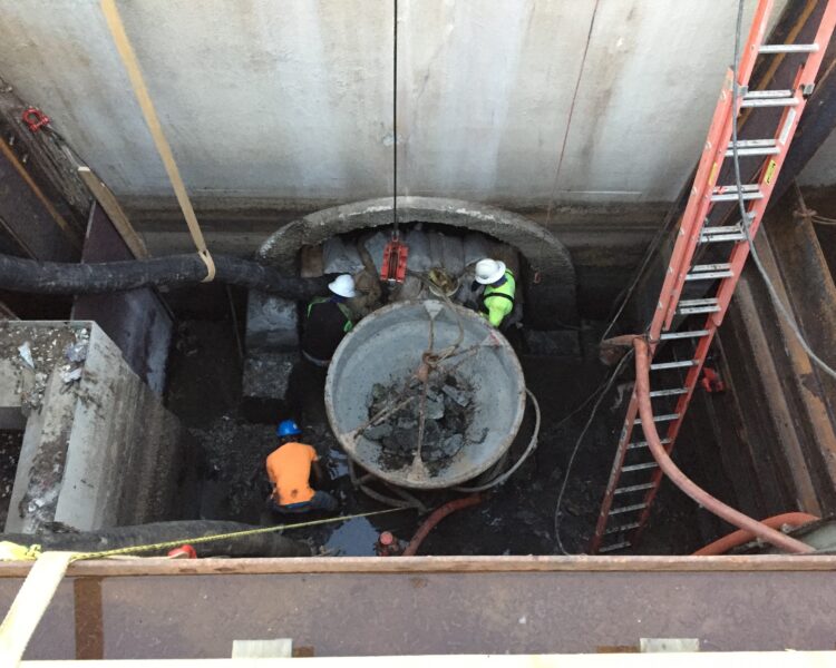 Three workers manage debris removal at a tunnel entrance.