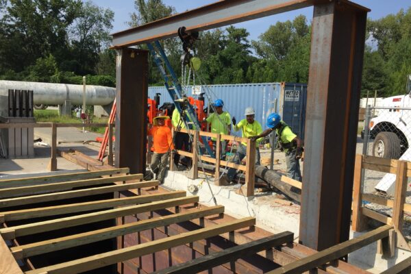 Unos trabajadores, equipados con material de seguridad, montan vigas de acero y tablones al aire libre.