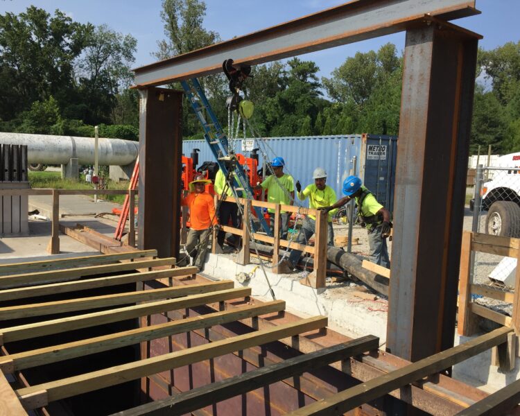Workers in safety gear assemble steel beams and planks outdoors.