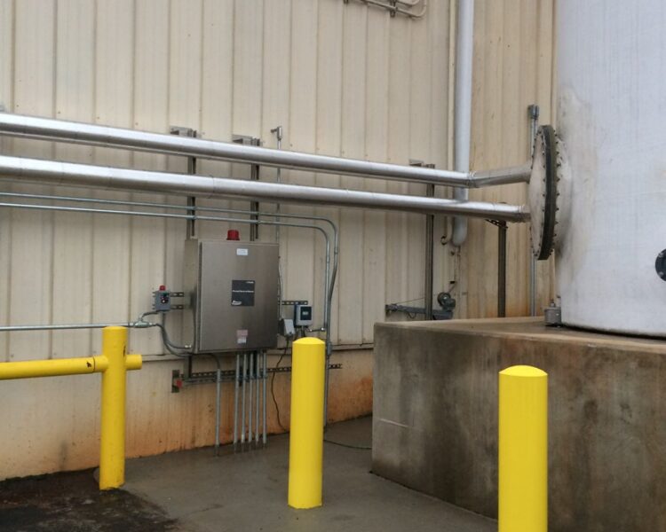 Metal pipes on beige building, yellow bollards and control panel.