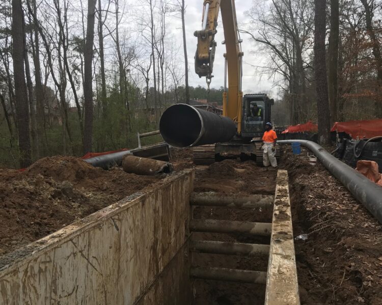 Los trabajadores utilizan una excavadora para bajar una tubería a una zanja en el bosque.