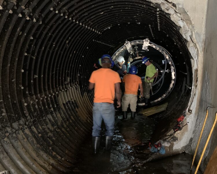 Unos obreros de la construcción, equipados con material de seguridad, trabajan en el interior de un túnel inundado.