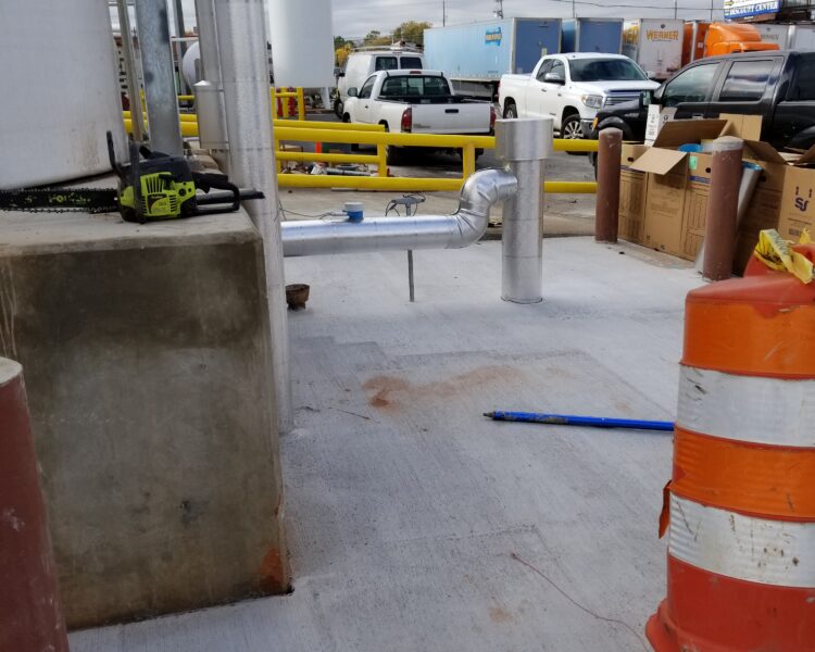 Concrete work area with materials, equipment, barrel, and vehicles.