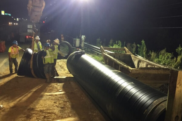 Los trabajadores instalan tuberías negras por la noche bajo una luz intensa.