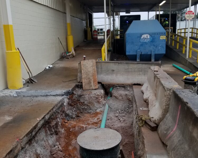 Trench, exposed pipes, barriers, dumpster, and railings at construction site.