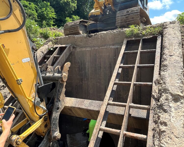 Una excavadora Kobelco amarilla sobre una plataforma de hormigón; unas escaleras conducen hasta los trabajadores que se encuentran abajo.