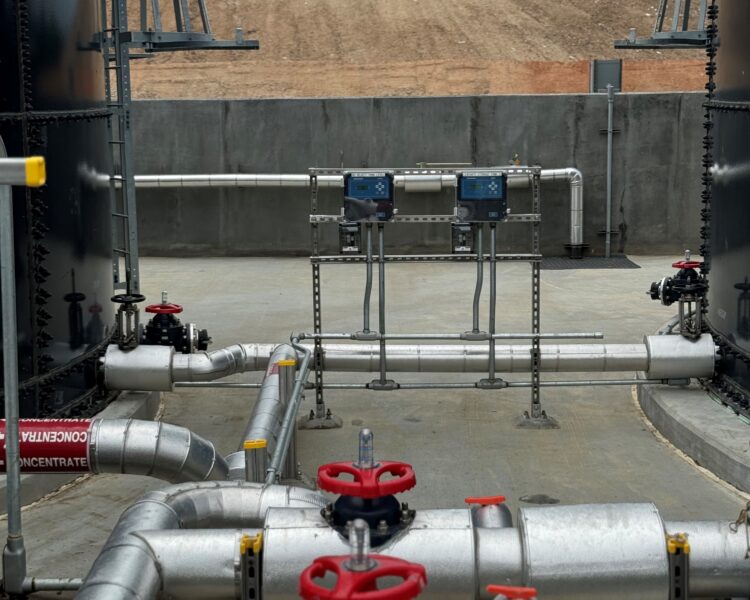 Tuberías industriales con manetas rojas entre grandes depósitos al aire libre.