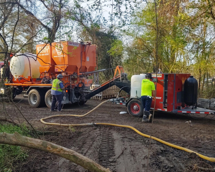 Workers spray hydroseed on soil from a large truck.