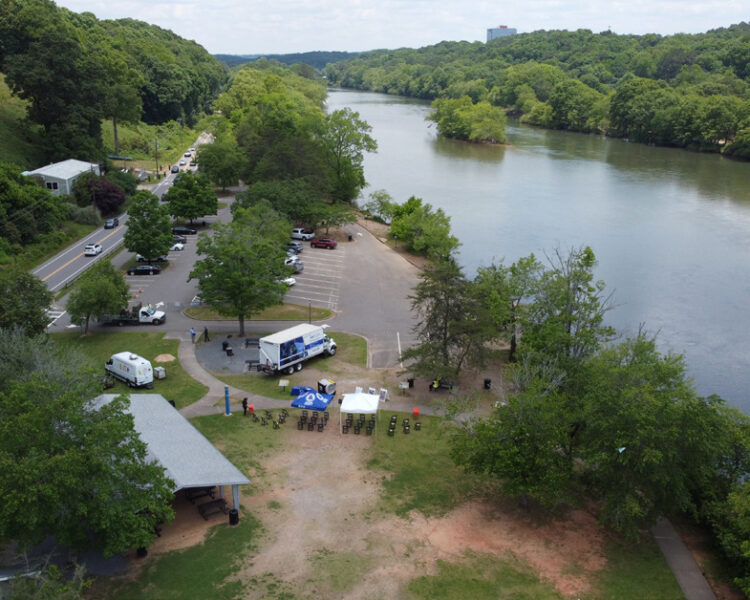 Aerial view: riverside park, parking lot, food trucks, tents.