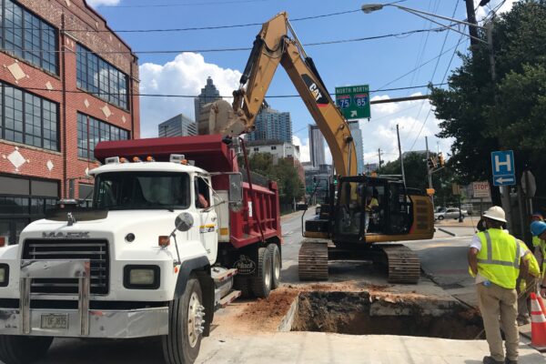 Un camión volquete, una excavadora y dos trabajadores en una obra municipal.