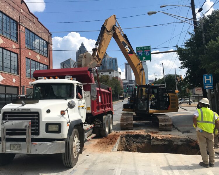 Un camión volquete, una excavadora y dos trabajadores en una obra municipal.