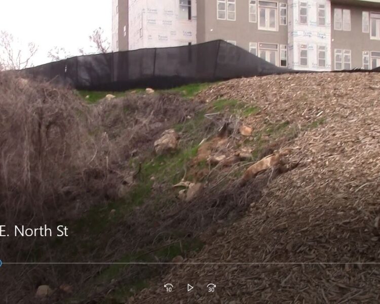 Wood chip-covered slope, silt fence above, unfinished building behind.