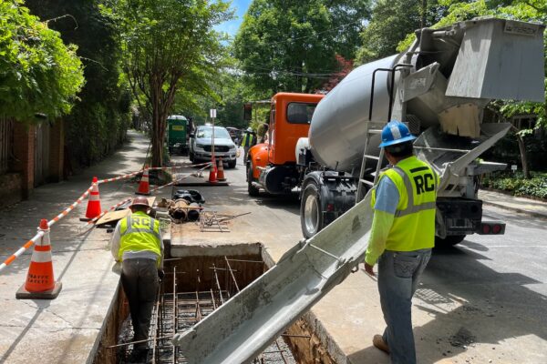 Unos obreros vierten hormigón en una zanja de la calle, cerca de las barreras de seguridad.