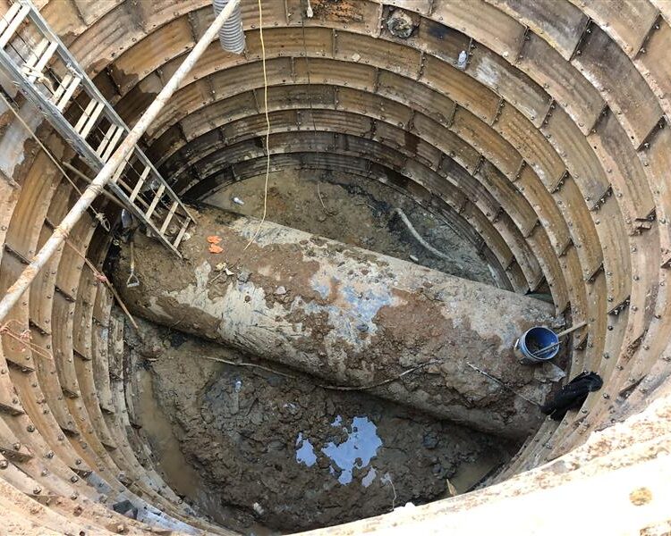 Circular pit with metal supports, pipe, ladder, bucket, mud.