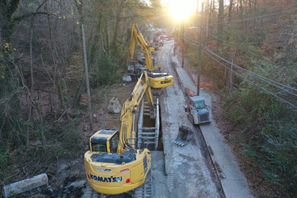 Excavadoras Komatsu en un camino boscoso al amanecer, con las líneas eléctricas a la derecha.