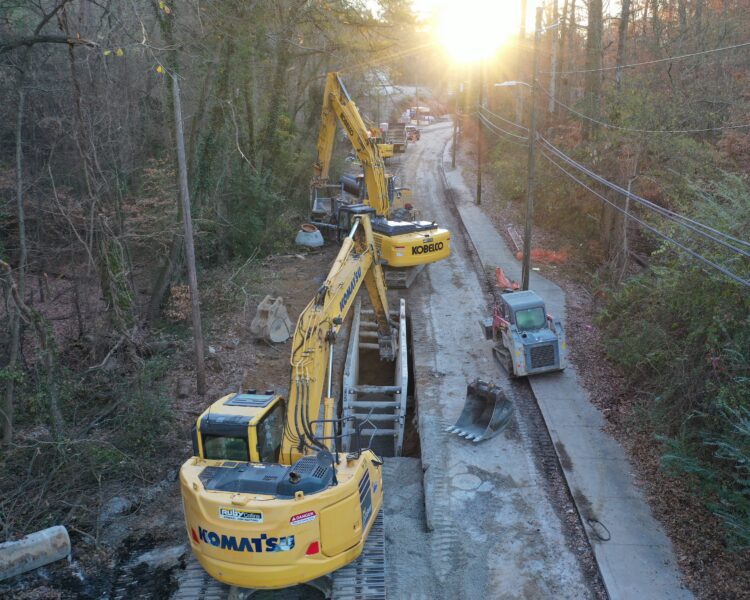 Excavadoras Komatsu en un camino boscoso al amanecer, con las líneas eléctricas a la derecha.
