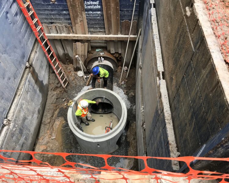 Los trabajadores instalan una gran tubería de hormigón en una zanja profunda y reforzada.