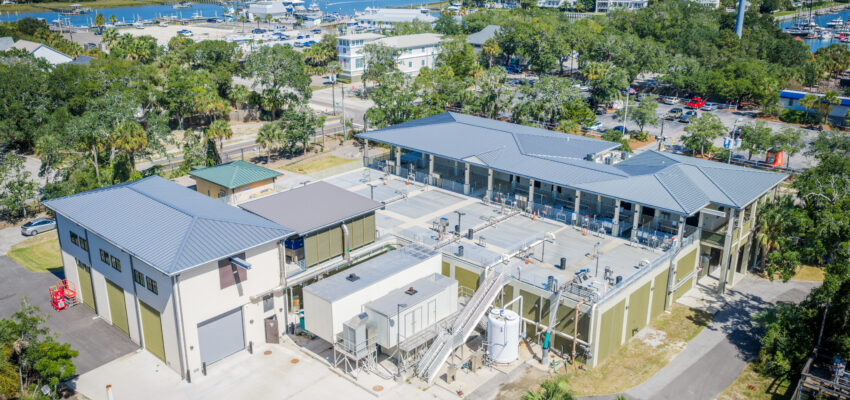 Aerial view of wastewater plant by water, boats, and trees.