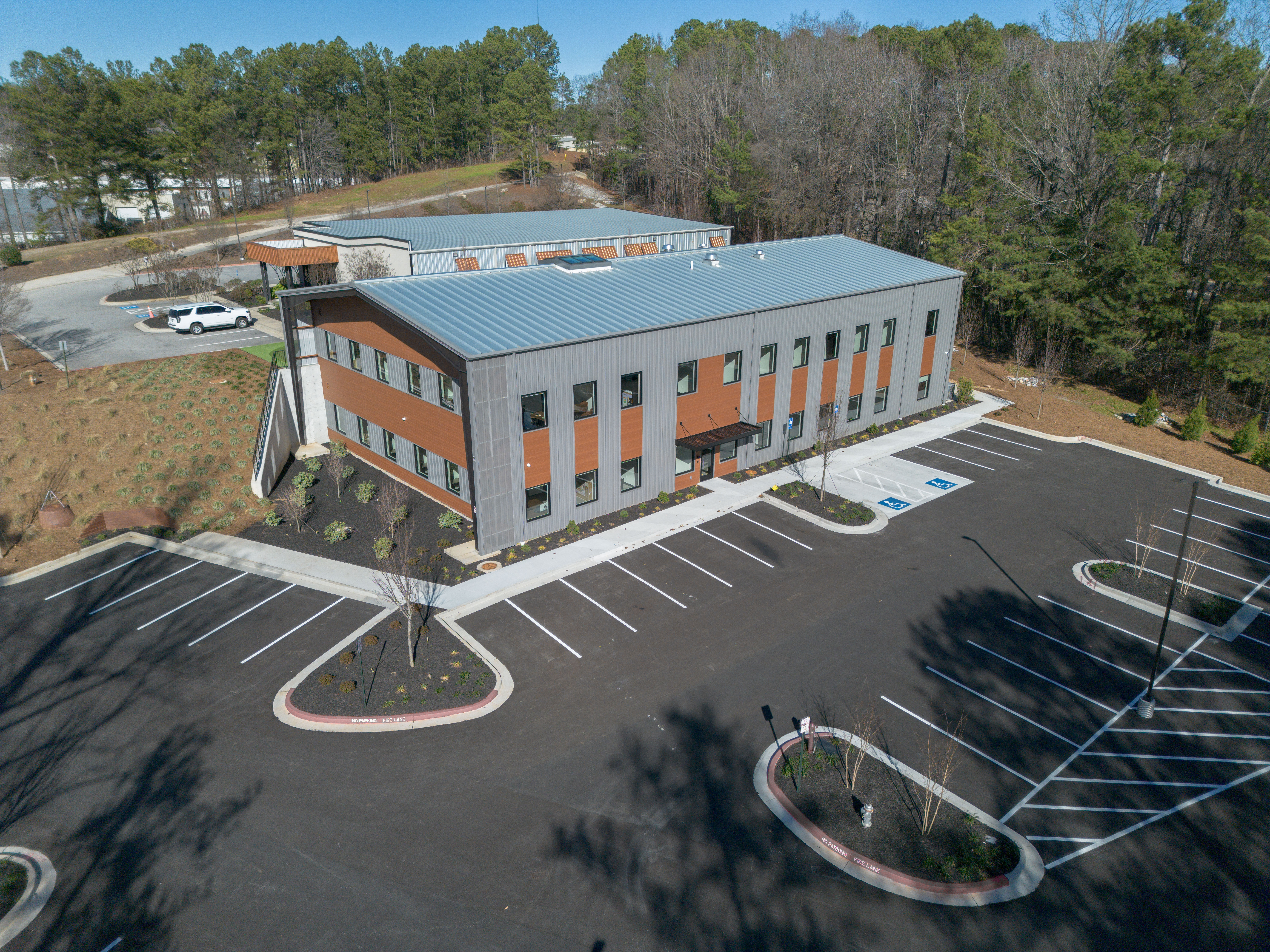Aerial view of a modern building with metal roof and an empty parking lot.