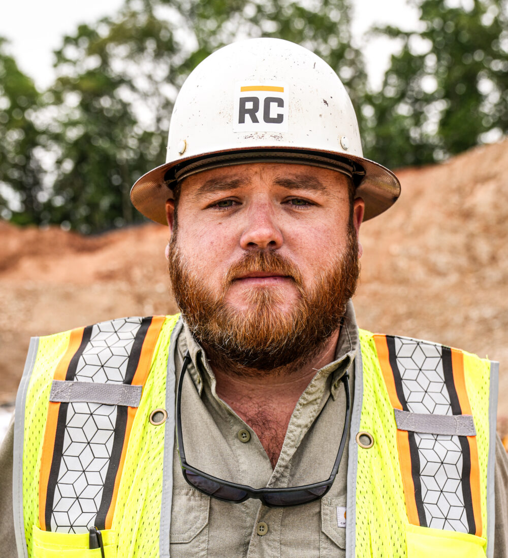 Bearded man in RC hard hat and yellow vest at construction site.