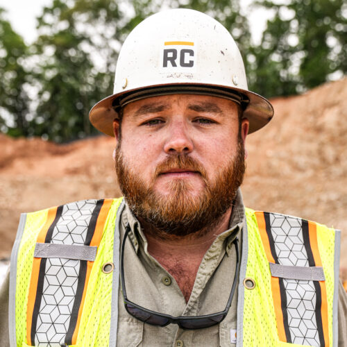 Bearded man in RC hard hat and yellow vest at construction site.