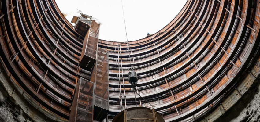 Looking up through a deep shaft as a crane lifts metal.